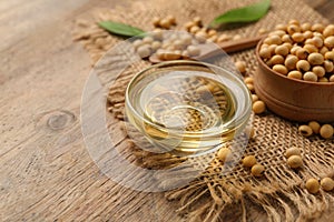 Glass bowl with oil and soybeans on wooden table, closeup