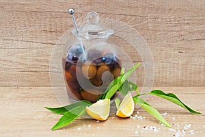 A glass bowl with olives in olive oil on a wooden background with lemon, sea salt. Traditional greek food.