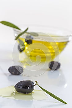 Glass bowl of organic olive oil and fres olive with leaves on white background