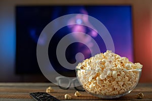 A glass bowl of popcorn, 3d glasses and remote control in the background the TV works. Evening cozy watching a movie or TV series photo