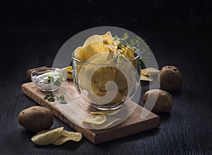 glass bowl of potato chips on a dark wooden background with sauce