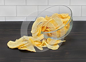 A glass bowl of potato chips spilling onto a tabletop