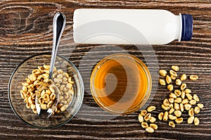 Glass bowl with puffed wheat, spoon, bottle of yogurt, honey, scattered puffed wheat on table. Top view