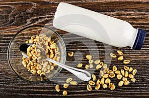 Glass bowl with puffed wheat, spoon, bottle of yogurt, scattered puffed wheat on wooden table. Top view