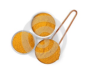 Glass, bowl and scoop with curry powder on white background, top view