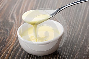 Bowl with sweet condensed milk, spoon with milk above bowl