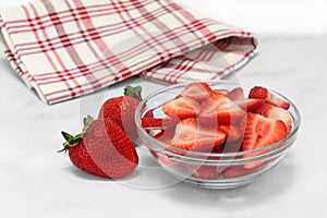 A glass bowl of sweet sliced strawberries with whole berries to the side