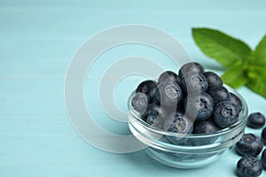 Glass bowl of tasty blueberries on color wooden table