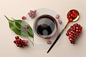 Glass bowl of tasty pomegranate sauce, fresh ripe fruit and spoon on white background, flat lay