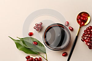 Glass bowl of tasty pomegranate sauce, fresh ripe fruit and spoon on white background, flat lay. Space for text