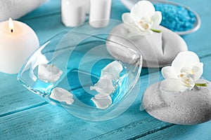 Glass bowl of water with flower petals and spa stones on table