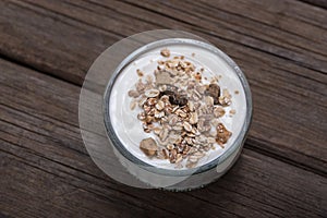 Glass bowl with white yogurt on old wooden desk with oatmeal on top