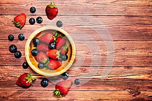 A glass bowls with strawberries and blueberries on a wooden table.