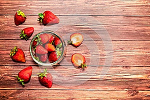 A glass bowls with strawberries on a wooden table.