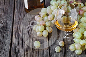 Glass of brandy with brush of grapes on table, harvest holiday