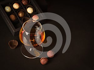 A glass of brandy and chocolate candy on a dark background. Alcoholic drink and elite chocolate food concept.