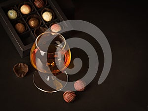 A glass of brandy and chocolate candy on a dark background. Alcoholic drink and elite chocolate food concept. photo