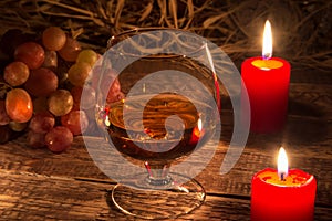 Glass with brandy or cognac, grapes and candle on aged wood table background. Close-up view.