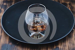 Glass of brandy with ice cubes/Glass of brandy with ice cubes on a black tray