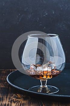 Glass of brandy with ice cubes/Glass of brandy with ice cubes on a black tray