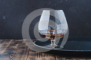 Glass of brandy with ice cubes/Glass of brandy with ice cubes on a black tray. Black background with copyspace