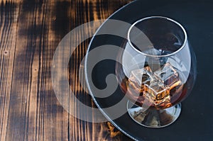 Glass of brandy with ice cubes/Glass of brandy with ice cubes on a black tray. Top view and copyspace
