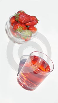 A glass of bright red raspberry-strawberry sweet cold drink with a cup of strawberries in the background