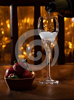 Glass of brut champagne bubbles wine in tulip glass and bowl with fresh strawberries on evening bar lights background