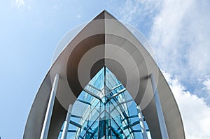 The glass building in the form of the ship against the blue sky with clouds