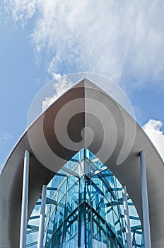 The glass building in the form of the ship against the blue sky with clouds