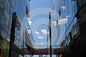 Glass building reflects. Street photography. Reflection of glass shopping centers between which lies a bridge. Blue sky with