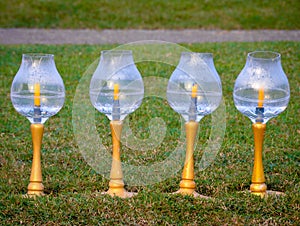 Glass candelabra with handles placed on an outdoor lawn.