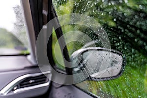 The glass of the car window and rear-view mirrors in raindrops. Abstract travel transport background