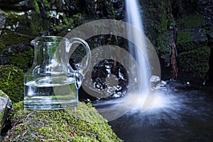 Glass carafe with water and waterfall in background