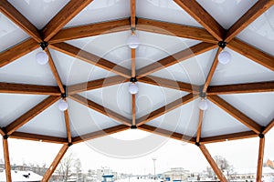 Glass ceiling with lanterns in a brown wooden gazebo outdoors in winter