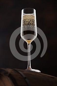Glass of champagne with bubbles on top of wooden barrel on black
