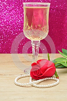 A glass of champagne displayed with a red artificial rose and a string of beads