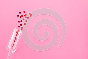 Glass of champagne with red hearts on a pink background. Valentines background, love, date concept with copy space, flatlay photo