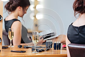 Glass of champagne standing on table near woman reading magazine