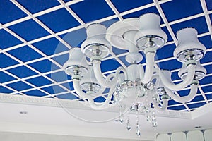 Glass chandelier on the ceiling. Stylish blue ceiling, divided into squares.