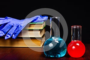 Glass chemical flasks with liquid and several textbooks on a dark wooden table. Class in chemistry, school, student