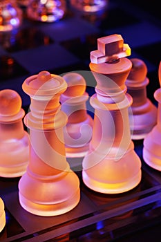 Glass chess on a chessboard lit by blue and orange light