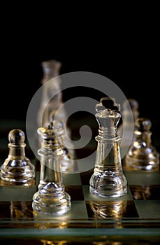 Glass chess pieces are defending the king on board in dark