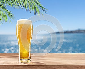 Glass of chilled beer on table and blurred sparkling sea at the background. Place for your product or brand name display