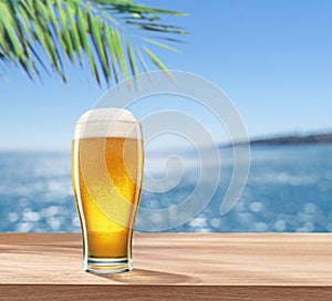 Glass of chilled beer on table and blurred sparkling sea at the background. Place for your product or brand name display