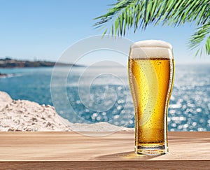 Glass of chilled beer on table and blurred sparkling sea at the background. Place for your product or brand name display
