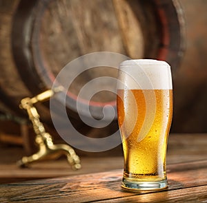 Glass of chilled beer and wooden beer cask at the background
