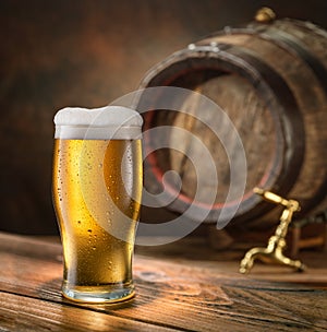 Glass of chilled beer and wooden beer cask on the background