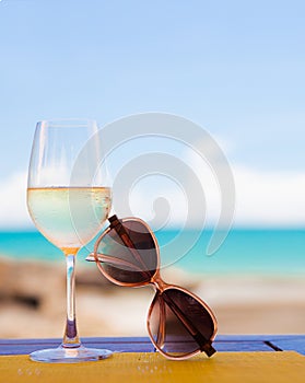 Glass of chilled white wine and sunglasses on table near the beach photo