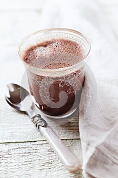 Glass of chocolate milkshake on bright wooden background.